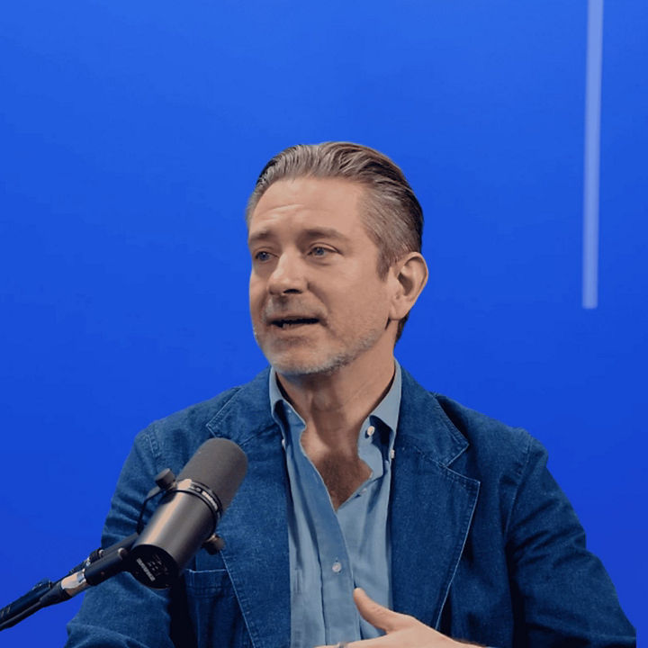 Person speaking into a microphone in a studio, seated against a blue background with vertical light accents