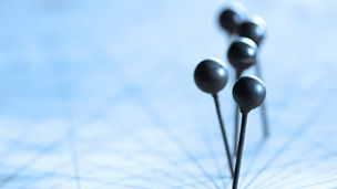 Nahaufnahme von schwarzen Stecknadeln auf einer Karte mit Linienmuster im Hintergrund.