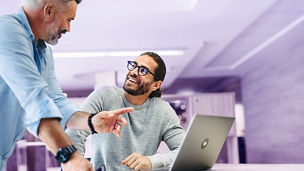 Successful businessmen smiling happily while working together in a co-working office. Two cheerful businessmen using a laptop while working on a new project.