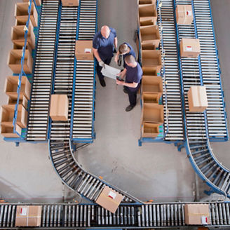 Workers meeting among boxes on conveyor belts in distribution warehouse