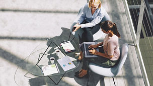 Two people working at an outdoor table with a laptop and documents