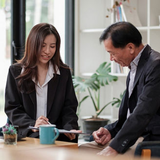 Two people reviewing documents together at a table in a bright office setting.