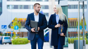 Two people walking next to a tall glass building