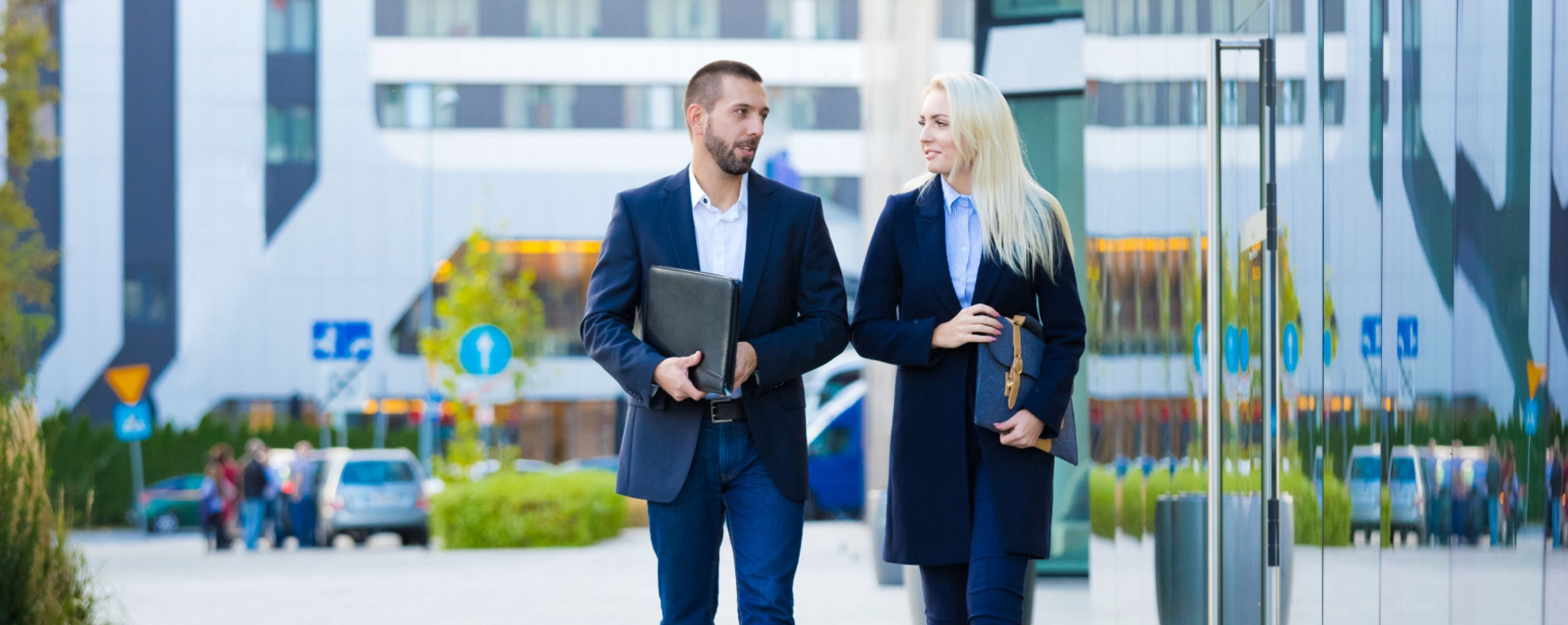 Two people walking next to a tall glass building