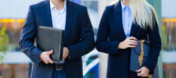Two people walking next to a tall glass building