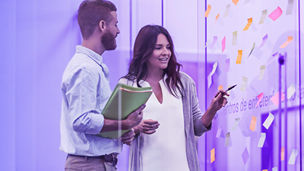 Twee collegas met elkaar in overleg voor een raam met notes er opgeplakt