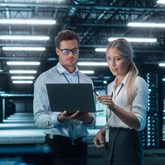Two professionals reviewing data on a laptop in a modern data center.