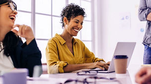 Black business woman using a laptop in a meeting with her team. Happy business woman sitting in a boardroom with her colleagues. Creative business people discussing a project in an office.