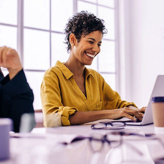 Business woman using a laptop in a meeting with her team. Happy business woman sitting in a boardroom with her colleagues. Creative business people discussing a project in an office.