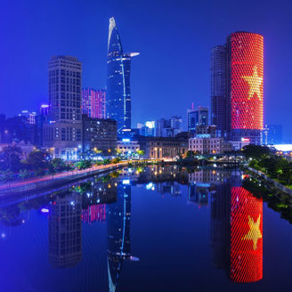 Vietnam city skyline with illuminated high‑rise buildings reflected in a river, featuring a purple gradient overlay along the left side of the image