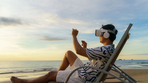 Young Asian man using virtual reality glasses for business meeting on the tropical beach over beautiful sea and sky background