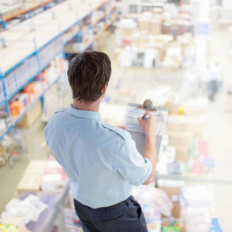Person reviewing inventory on a clipboard in a warehouse with shelves and stored goods.