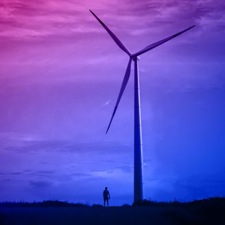 A wind turbine against a dark sky, a small silhouette of a man next to it