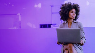 Woman with afro holding a laptop in the office, looking to the left