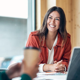 woman sitting at table with laptop and talking to other person
