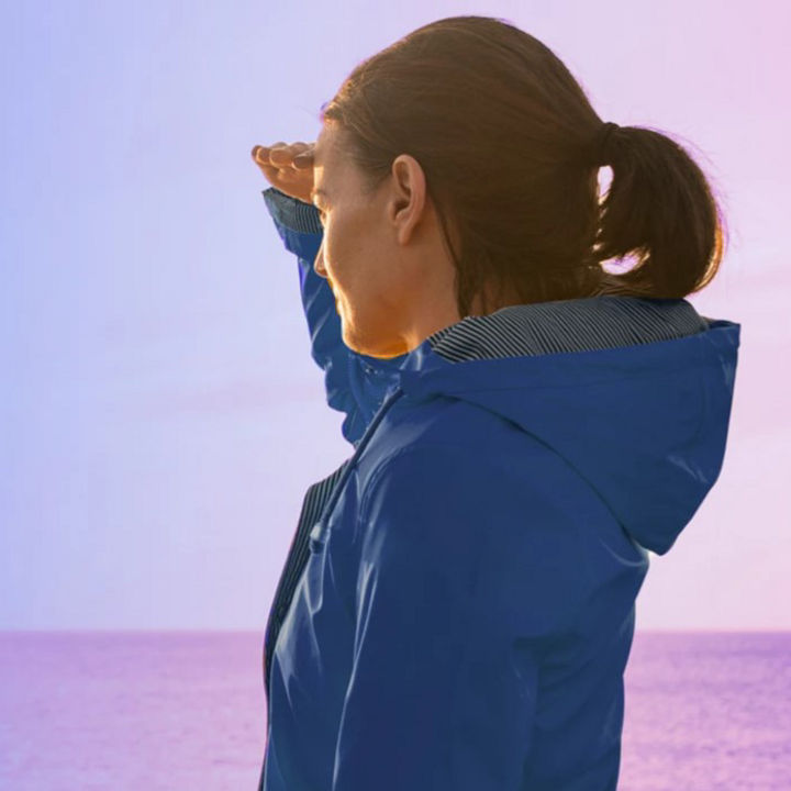 Woman in blue jacket looking at sunset across water banner