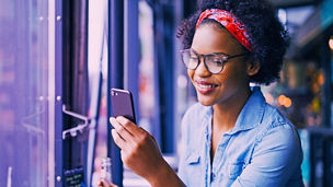 Attractive young African woman smiling and reading texts on a cellphone while sitting alone at a counter in a cafe enjoying a meal