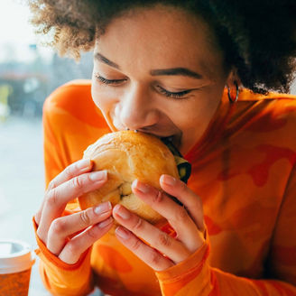 Person taking a bite of a sandwich with a takeaway coffee cup on the table.