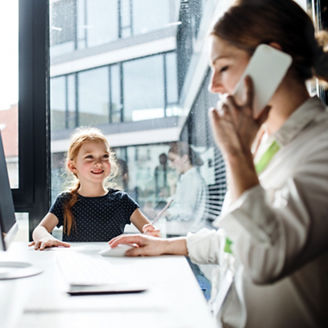 A businesswoman with a small daughter sitting in an office, working.