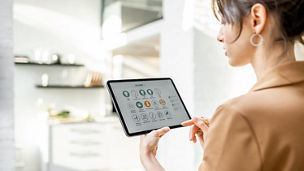 Woman controlling smart home devices using a digital tablet with launched application in the white living room. Smart home concept