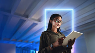 Woman wearing glasses reading tablet in dimly lit office