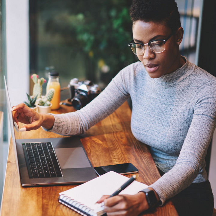 Woman with laptop writing in notepad