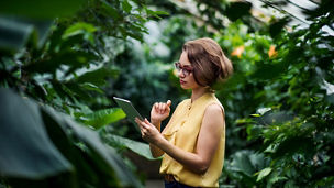 A young woman standing in greenhouse in botanical garden, using tablet.