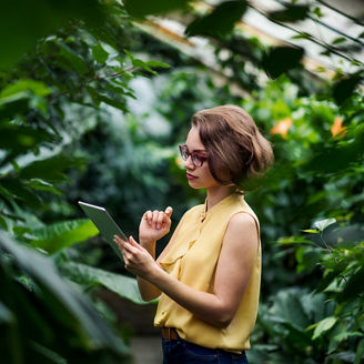 A young woman standing in greenhouse in botanical garden, using tablet.