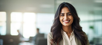 Successful indian businesswoman standing in creative office and looking at camera while smiling. Portrait of beautiful woman standing in front of business team at modern agency with copy space.