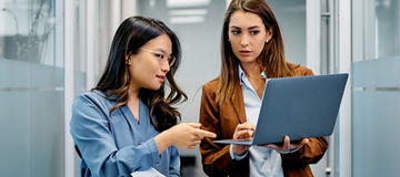 Young businesswomen cooperating while working on laptop in hallway.