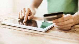 Young man using credit card with digital tablet at home