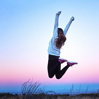 Young woman jumping and raising her arms at sunset