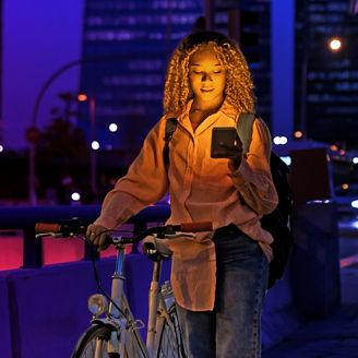Jonge vrouw kijkt op haar telefoon terwijl ze haar fiets aan de hand heeft